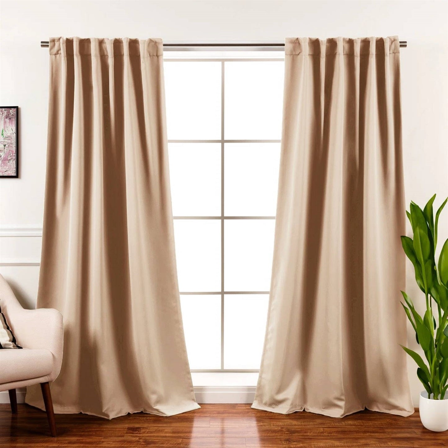 Beige curtains hanging in front of a window with a plant and chair in the foreground.