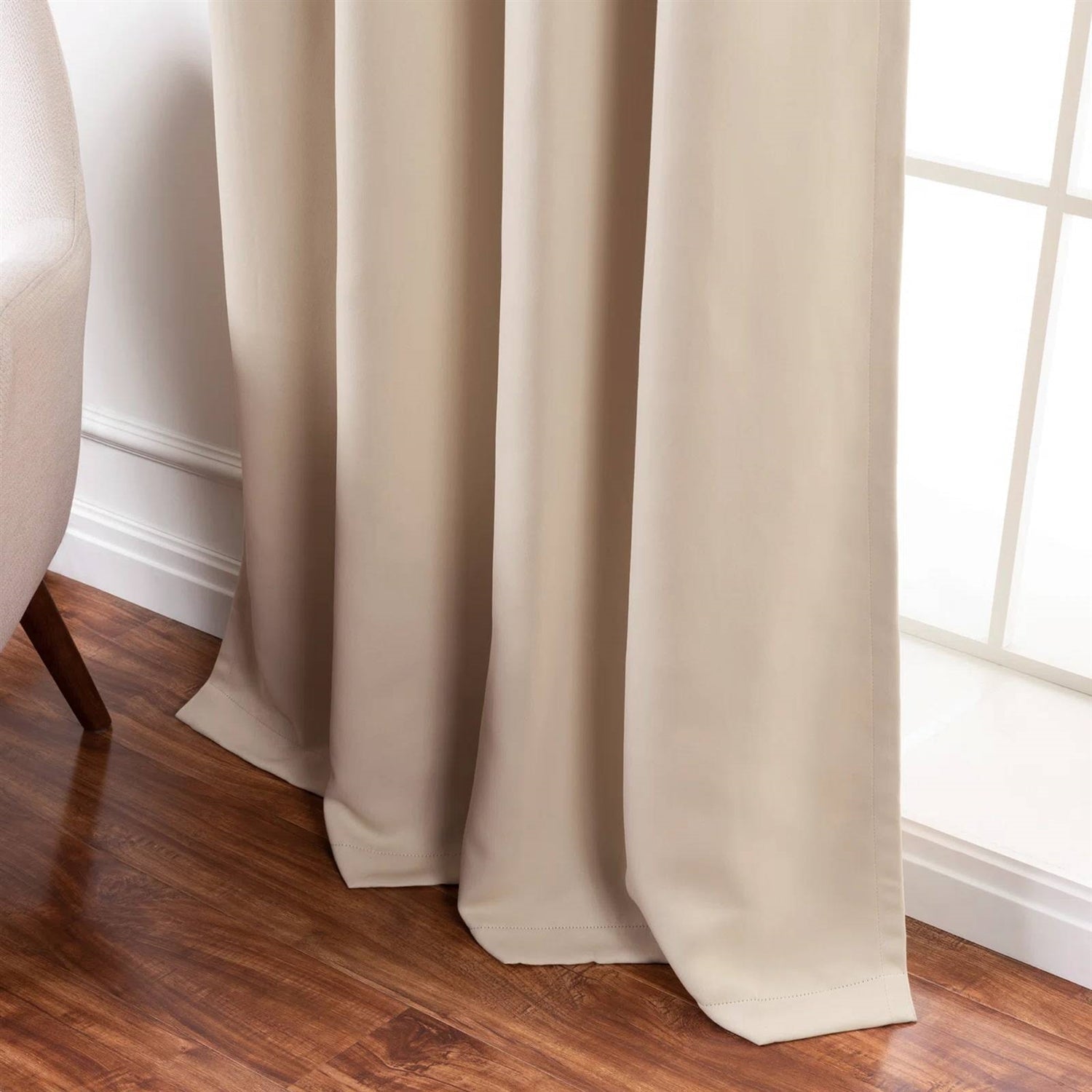 Beige curtains hanging by a window on a wooden floor.