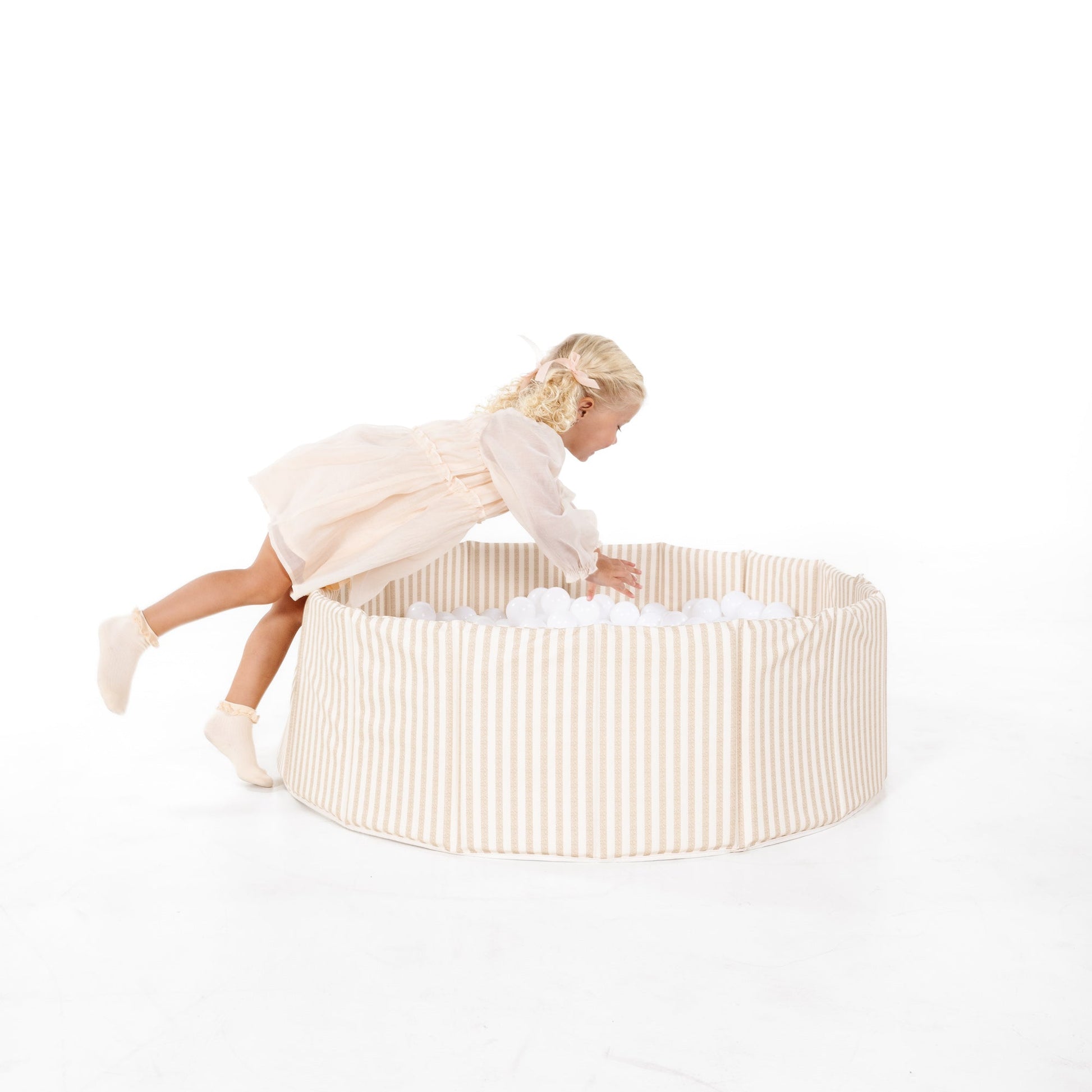 Child playing in a round, beige fabric playpen on a white background