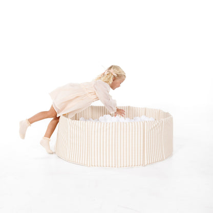 Child playing in a round, beige fabric playpen on a white background