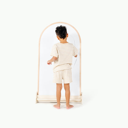 Child wearing a striped outfit standing in front of a mirror on a white background