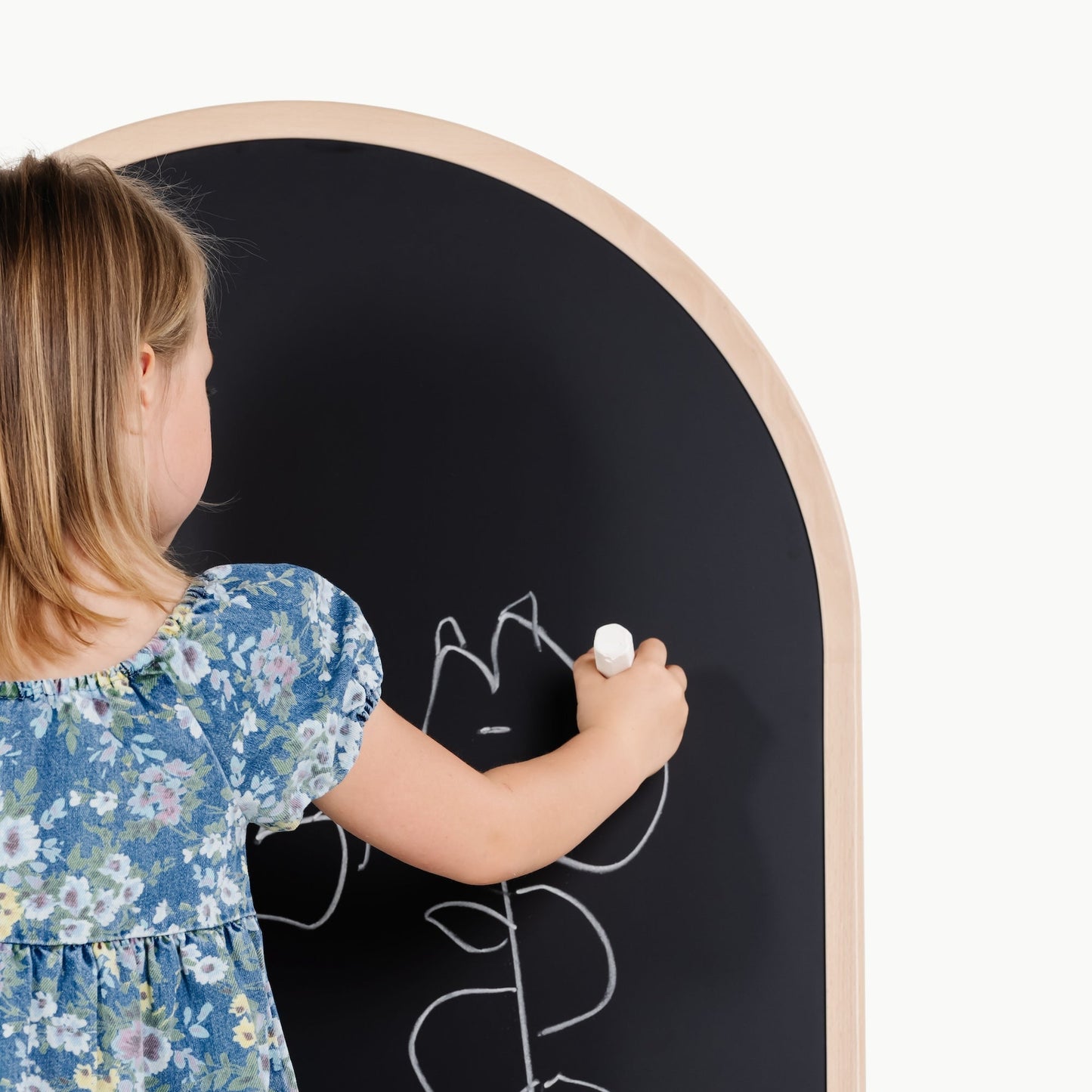 Child drawing on a round blackboard with a white chalk.