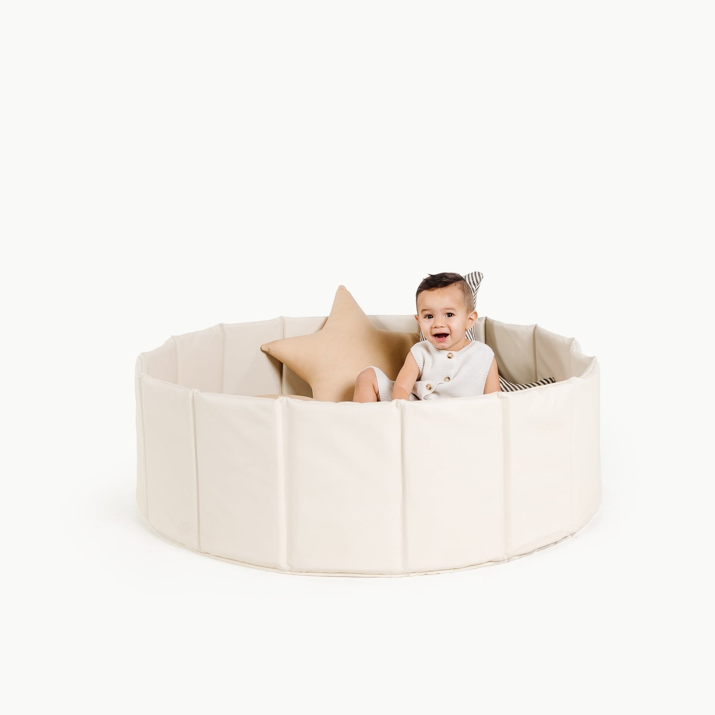 Baby sitting inside a round beige playpen with a white background