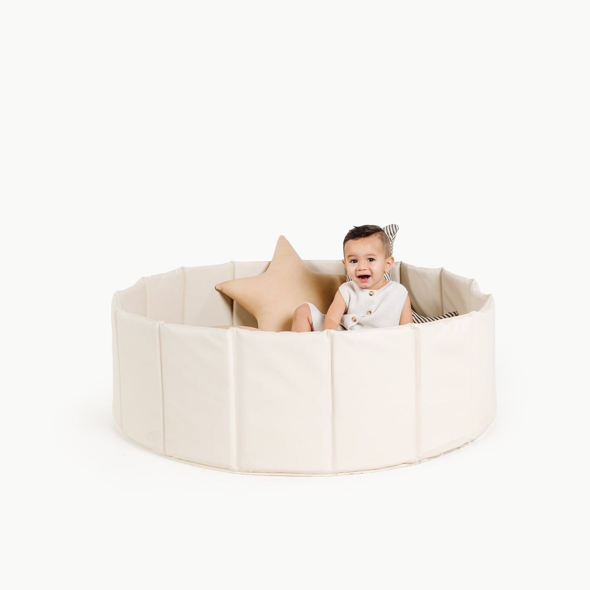 Baby sitting inside a round beige playpen with a white background