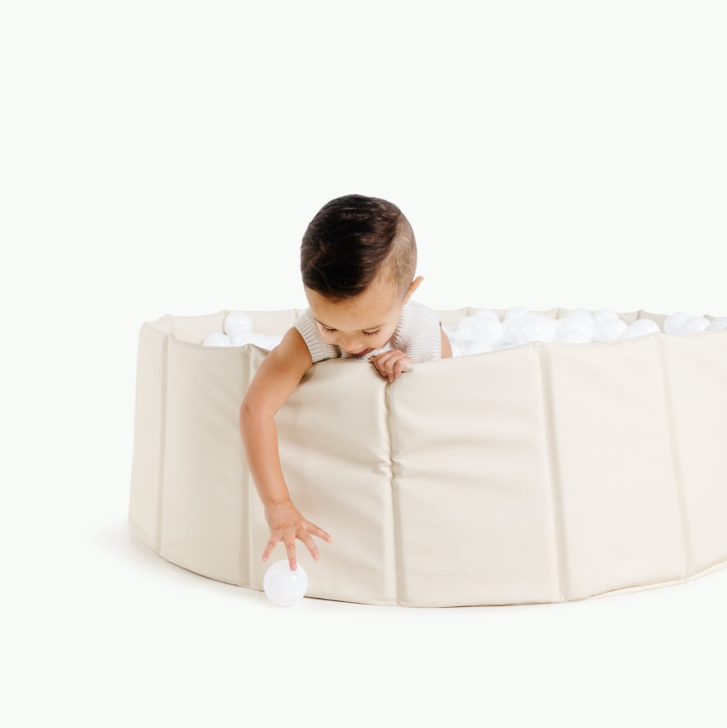 Child playing with a round beige playpen on a white background