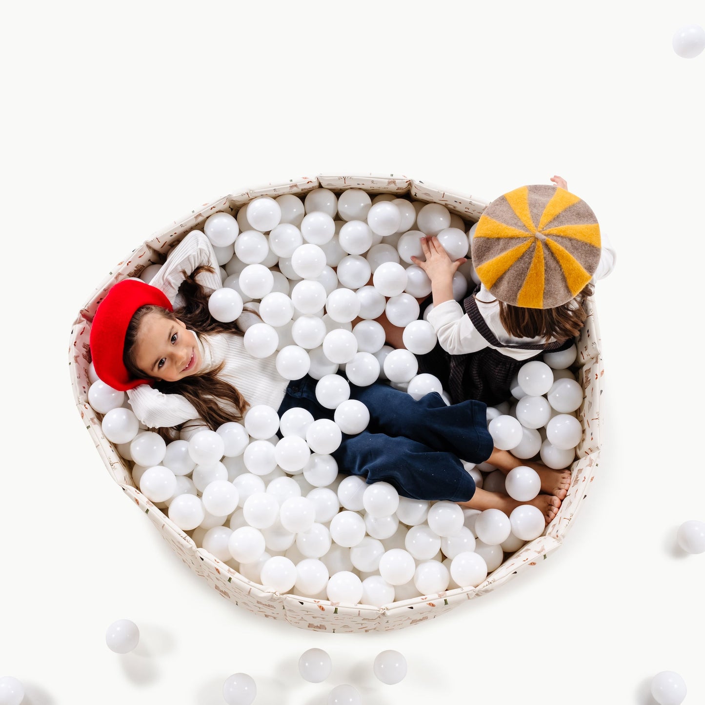 Two children playing in a ball pit with white balls on a white background