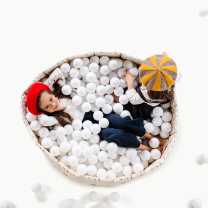Two children playing in a ball pit with white balls on a white background