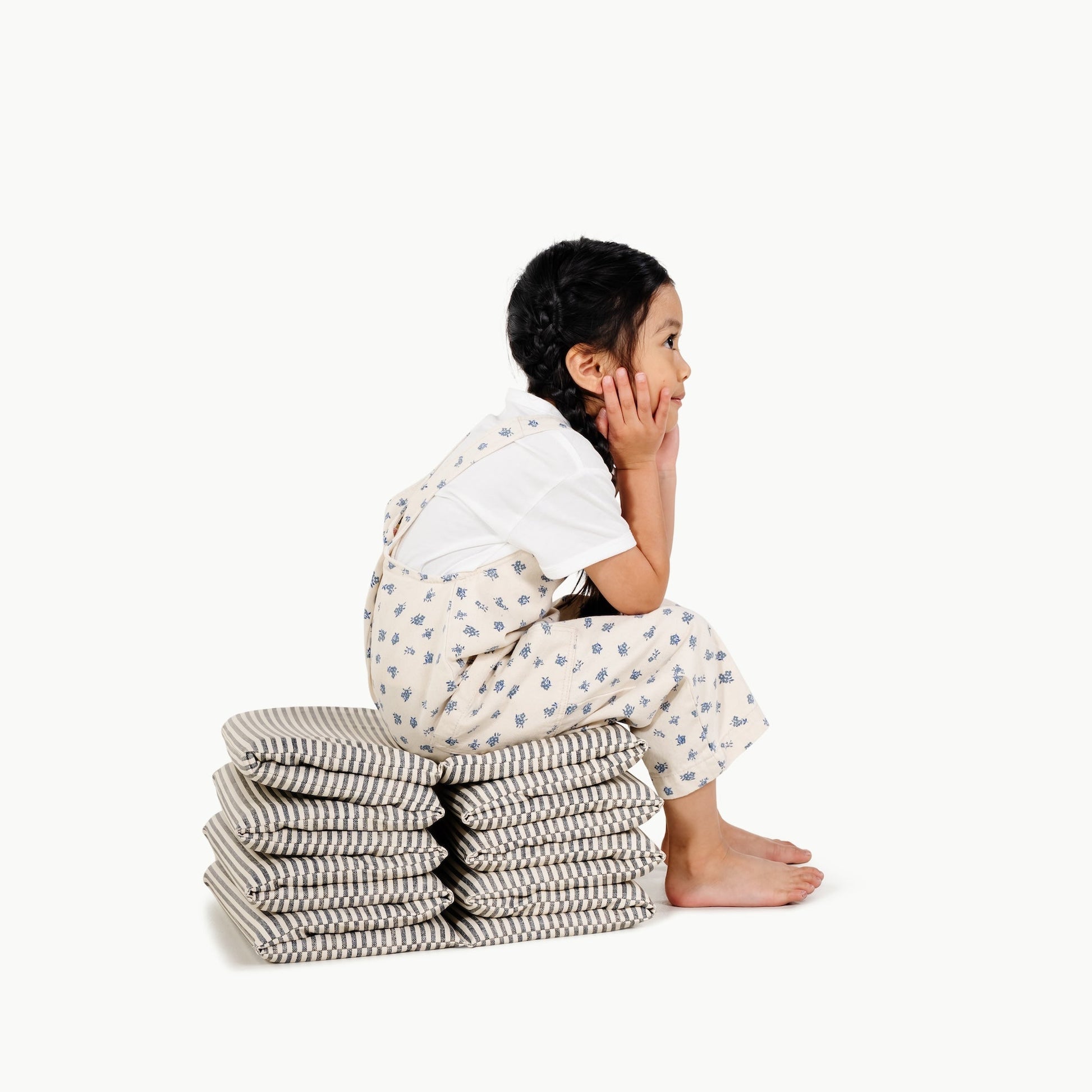 Child sitting on a stack of folded clothes against a white background