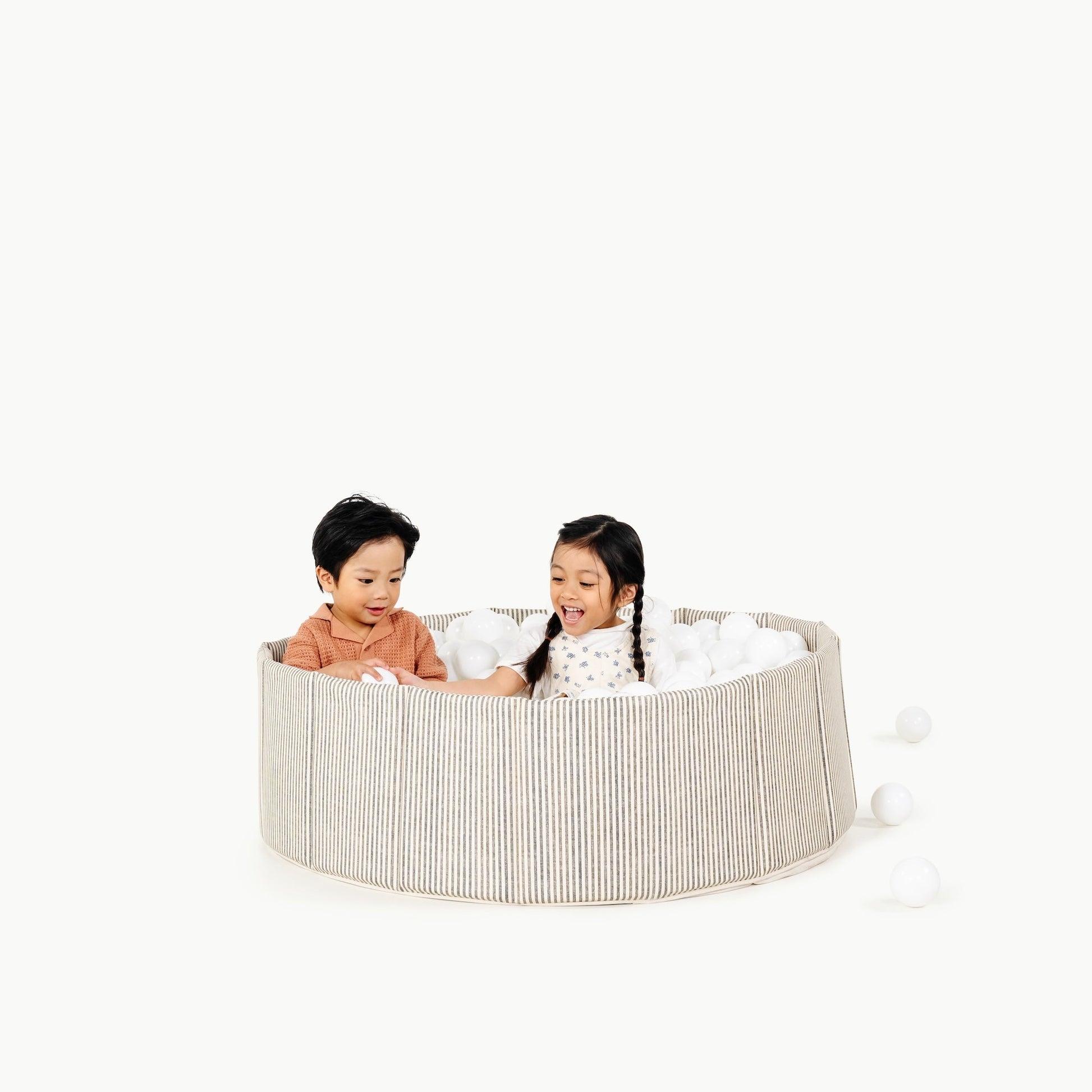 Two children playing inside a round, beige playpen on a white background