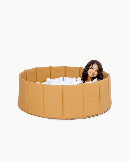 Person playing with a beige inflatable pool filled with white balls on a white background