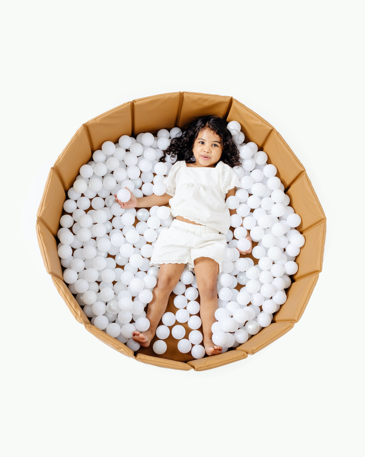 Child playing in a cardboard ball pit filled with white balls on a white background