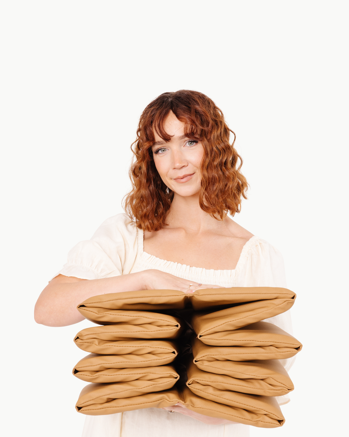 Woman holding a stack of brown pillows against a white background
