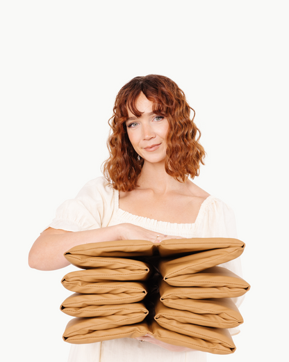 Woman holding a stack of brown pillows against a white background