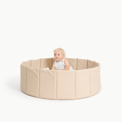 Child sitting inside a beige playpen on a white background