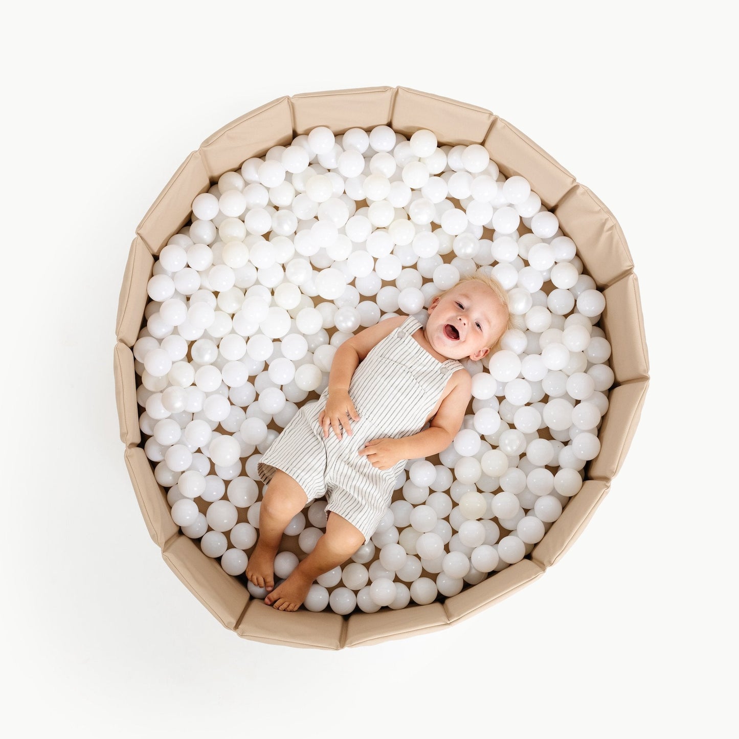 Baby lying on white ball pit balls inside a cardboard box on a white background