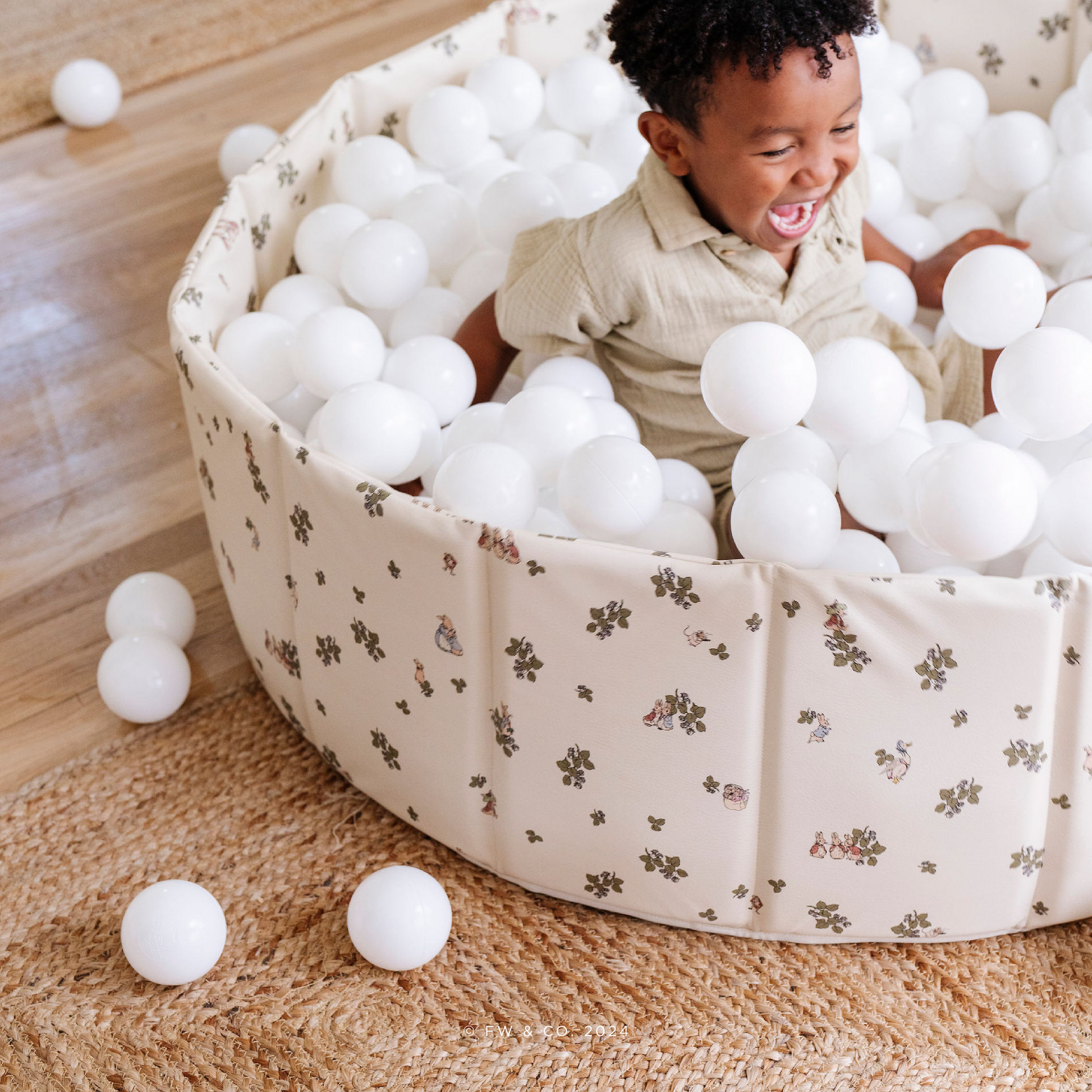 Child playing with white balls in a large paly pen on a wooden floor