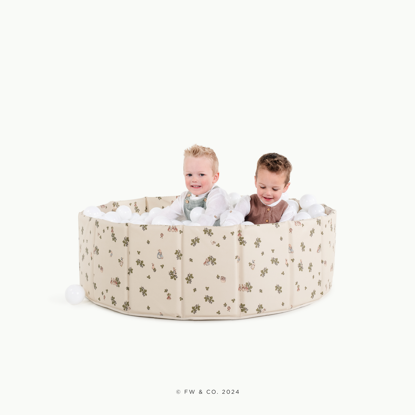 Two children playing inside a round, beige playpen with a floral pattern on a white background.