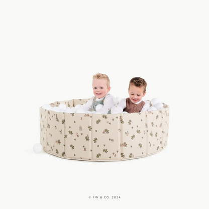 Two children playing inside a round, beige playpen with a floral pattern on a white background.