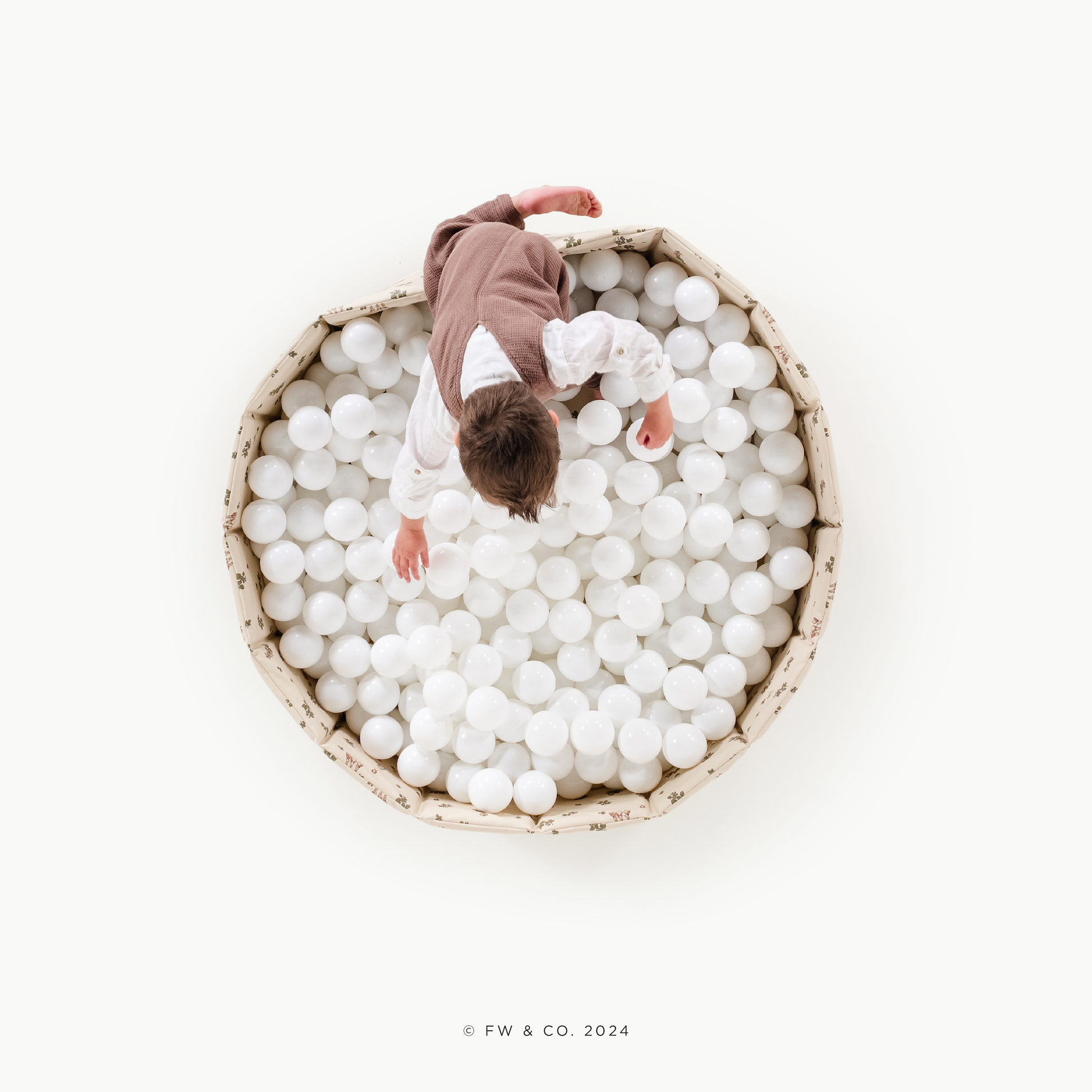 Two children playing in a large bowl filled with white balls on a white background.