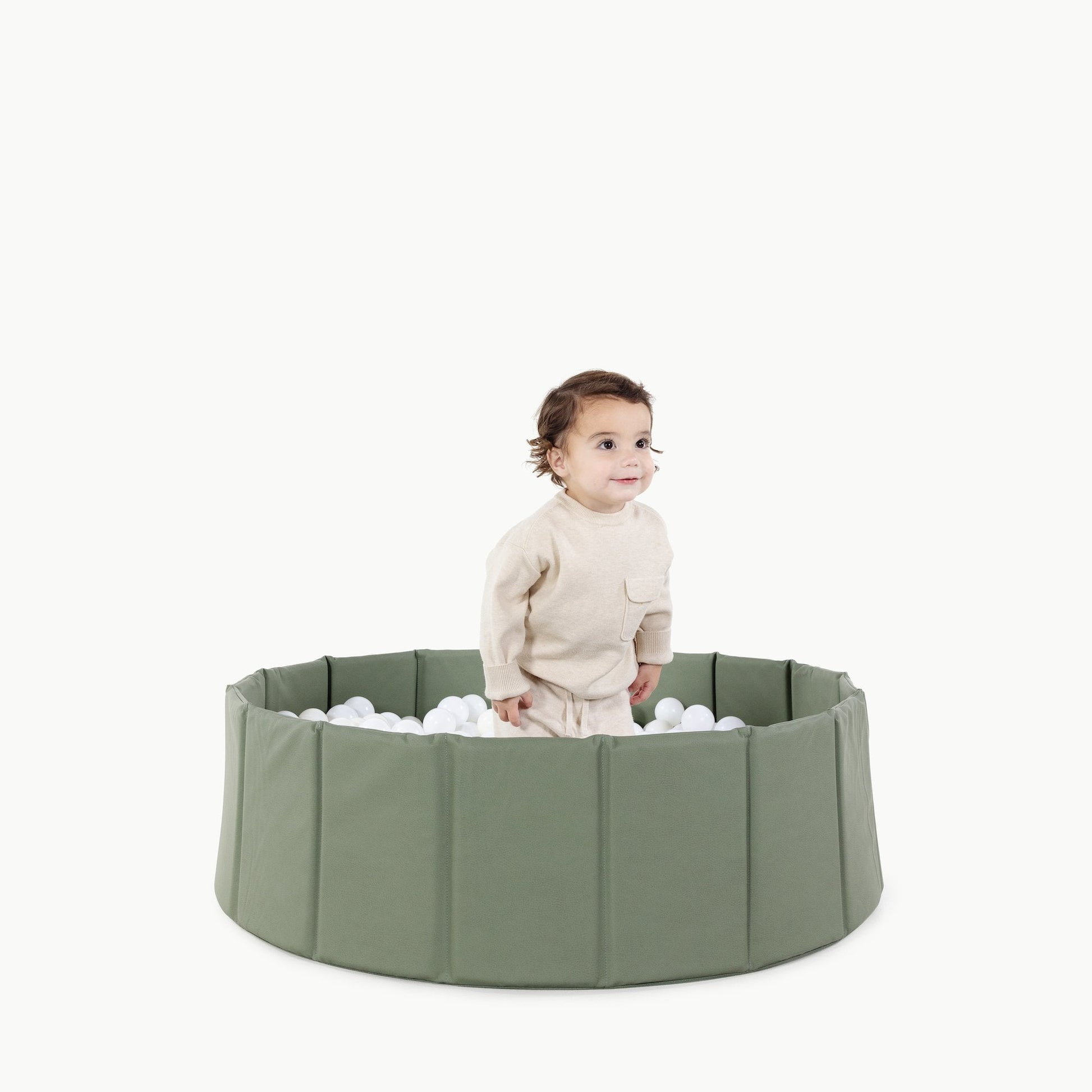 Child playing with a green playpen filled with balls on a white background