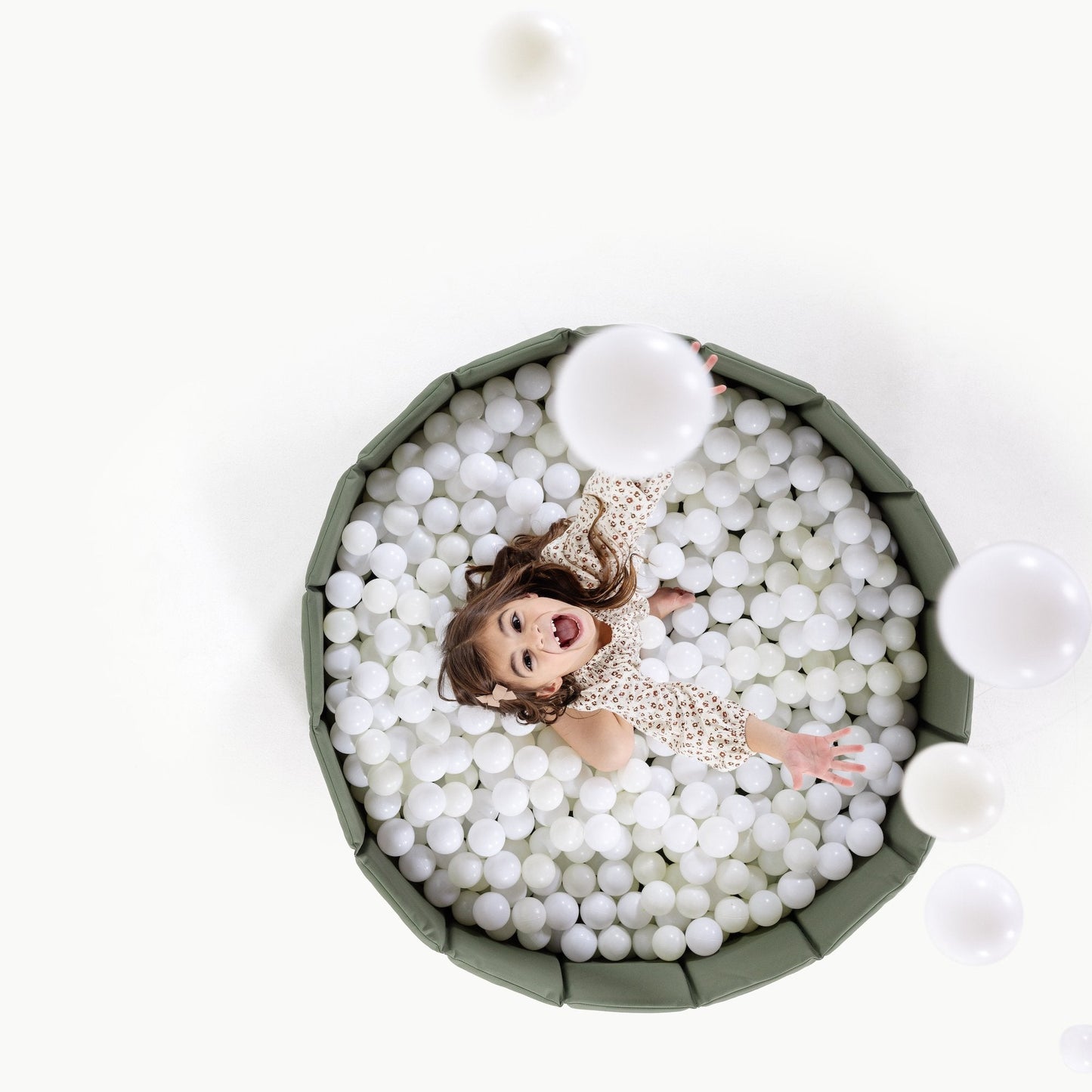 Doll in a ball pit with white balls on a white background