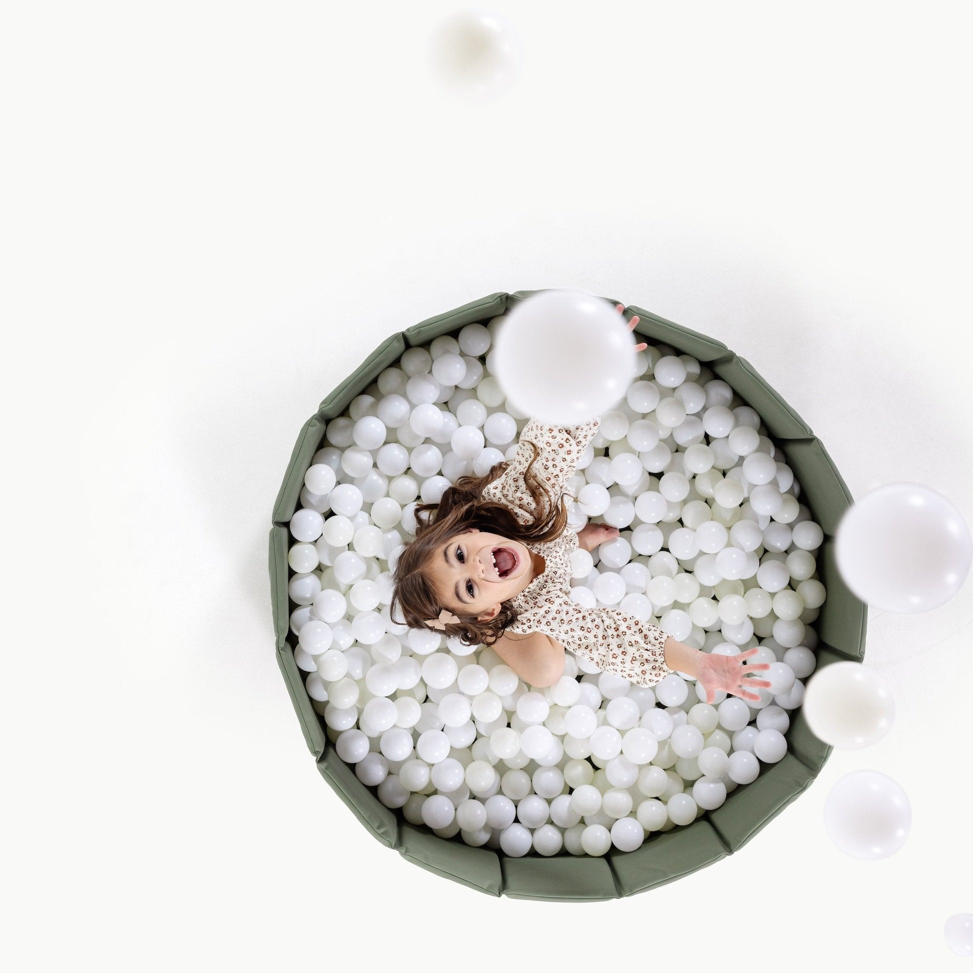 Doll in a ball pit with white balls on a white background